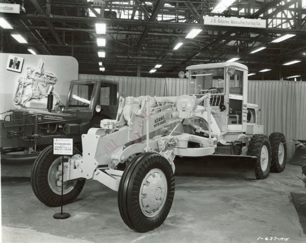 Motor grader on display in the Industrial Power Exhibit for Allied Equipment Manufacturers at International Harvester's Melrose Park Works. The sign in front of the machinery reads: "No.512 Adams Motor Grader powered by UD-14A Diesel Power Unit; 68.4 Max. H.P. at 1350 R.P.M.; Total Weight 23,400 lbs."