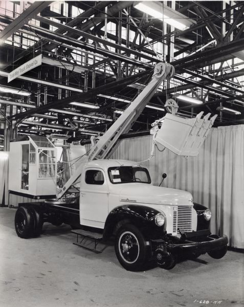 View of right side of an International K-5 truck with a crane attachment on display at Melrose Park Works as part of the Industrial Power Exhibit for Allied Equipment Manufacturers. The sign above the truck reads: "'Quick Way' Truck Shovel Co."