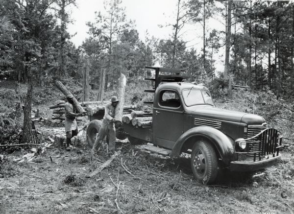 Two men load logs from a clearing onto the bed of an International KB-5 Pulpwood Special truck owned by the Johnson-Manville Corporation. The truck had a 158-inch wheelbase.