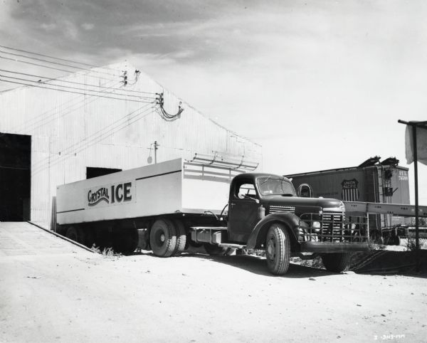 An International KB-8 truck with a semitrailer for hauling ice. The truck is parked in a loading area near a warehouse building. The truck was owned by the Crystal Ice Company and sold by the O.S. Stapley Company. Union Pacific, Pacific Fruit Express railroad car #74588 is behind the truck.
