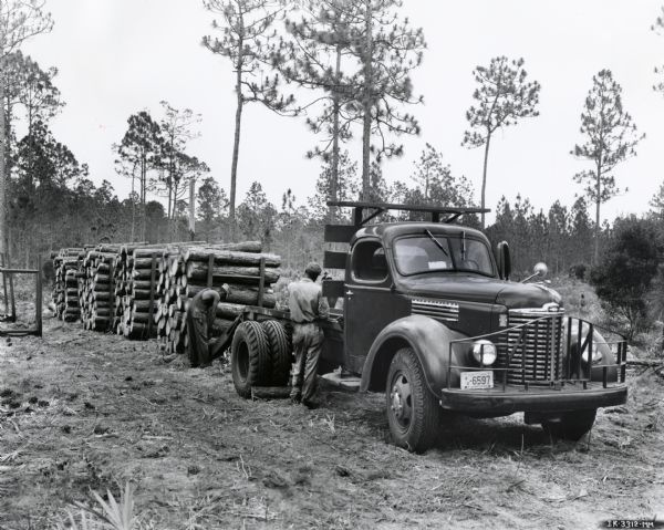 Men load logs onto the back of an International KBS-6 Pulpwood Special truck in a wooded area. The original caption reads: "The International KBS-6 pulpwood special motor truck is doing a most satisfactory job of hauling in the tough conditions that prevail in this type of work for two owners in the vicinity of Brunswick, Georgia. One of the trucks owned by W.T. Sumler, 1628 Johnson Street, Brunswick, is shown out in the woods, 43 miles south of Brunswick, taking its two loaded pallets. The total load of these two pallets, which are rectangular sleds with a tubular upright at each corner, is two and one-half pulpwood units or about three cords. Mr. Sumler is shown in one of the illustrations supervising the winching of loaded pallets up on the truck over two sled runners fastened to the rear of the truck. The other International KBS-6 pulpwood special motor truck, which is owned by George Sears of Hortense, Georgia, is shown also with a load of two pallets or two an done-half units...plant of the Brunswick Pulp & Paper Company."