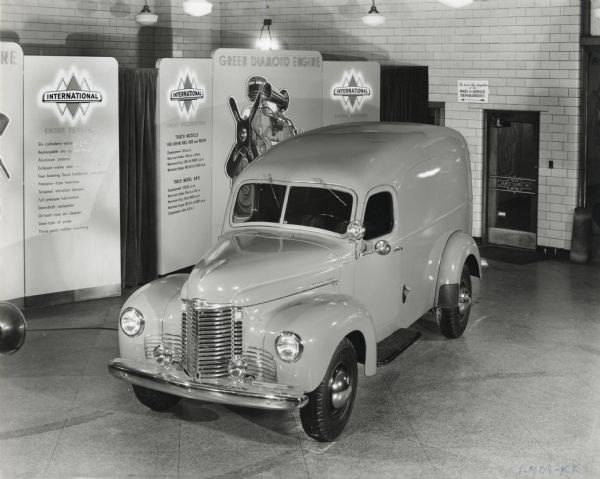 An International KB-5 truck on display, parked in front of signboards with informational materials. The signs advertise the "Green Diamond Engine" and list engine specifications and truck models.