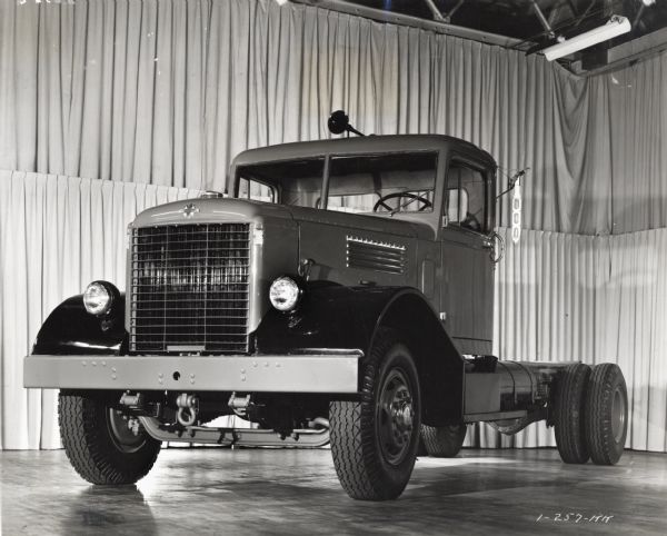 Three-quarter front view of an International truck on display in front of a hanging backdrop of curtains inside a building.