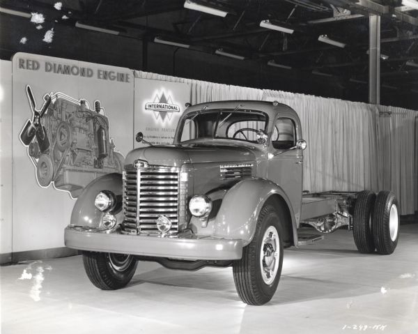 Three-quarter front view of an International truck on display inside a building. A backdrop and a display with information about the Red Diamond engine are behind the truck.