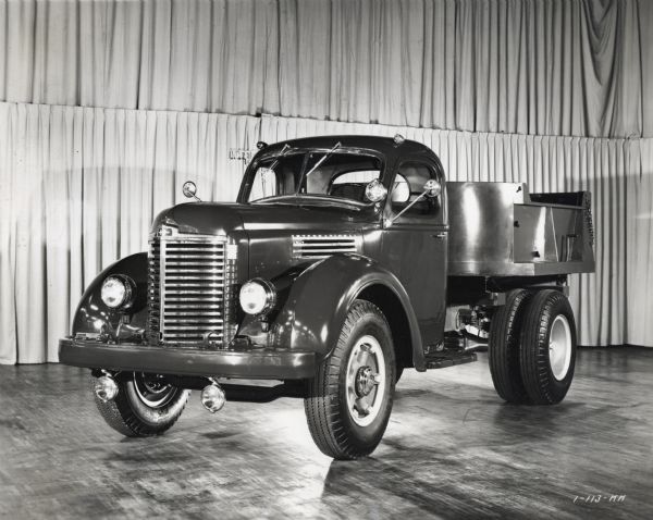 Three-quarter front view of an International KB-7 truck on display in front of a hanging backdrop of curtains inside a building.