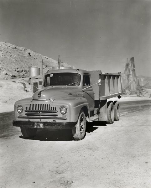 An International truck owned by the Vowell Material Company parked in a road. There are buildings and rocky terrain in the background. The original caption reads: "One of three new LF-170 six-wheel International dump trucks recently purchased by the Vowell Material Company, El Paso, Texas, is shown at the company's crushing and mixing plant near the Mexican border. It is shown loaded with crushed stone. Material for the crushing plant comes from a nearby small mountain consisting of a conglomerate of small stones and gravel. The output from three crushes is from 250 to 300 yards a day. The company also operates a hot mix plant and utilizes a fleet of International Transit-Mix trucks for making deliveries in El Paso. Its motor truck fleet consists of 40 units. Besides the three new LF-170's, an LF-190 has recently been purchased. Karl W. Kautz is plant superintendent."