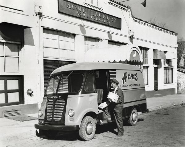 The driver of an International truck owned by Acme Laundry and Cleaners stands in the street near the driver's side door holding packages. The truck is parked in front of the company building. The original caption reads (in part): "One of two International LM-120 trucks with all-steel Metro bodies, recently purchased by the Acme Laundry Company of El Paso, Texas, is shown in front of the firm's attractive building at 905 East Missouri Street. The company has a fleet of 22 trucks, 17 of which are Internationals. It operates 17 laundry routes and 5 towel routes in El Paso and suburbs within a radius of 30 miles. Each truck averages 100 stops a day and travels an average of 35 miles. All trucks are finished in orange and two tones of blue . . . The 9-1/2 foot body also provides convenient arrangement of laundry bundles both in the payload compartment and on the engine cover for fast, efficient delivery and pick-up. The Acme Laundry Company was founded in 1909. B.G. Williams is president; R.L. Davis, Sr., vice president and manager; Jack Inman, Jr., secretary and sales manager; and P.P. Cruey, fleet supervisor."