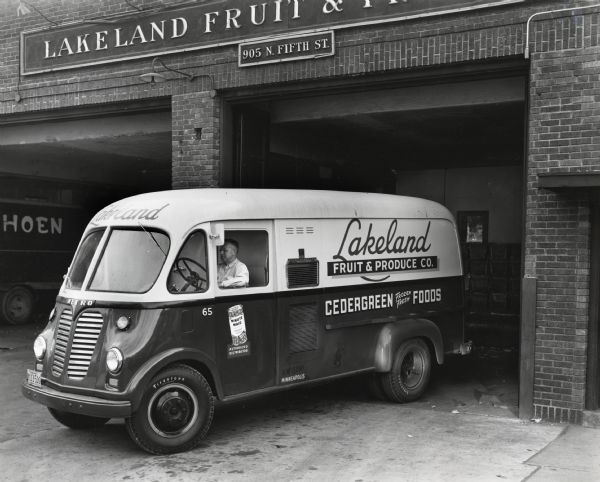 A man sits behind the wheel of an International LM-150 truck owned by the Lakeland Fruit & Produce Company. The truck is parked with its rear toward an open garage door at the company's main plant; the text on the side of the truck reads: "Minute Maid Authorized Seller" and "Cedergreen Frozen Fresh Foods." The original caption reads, "The Lakeland Fruit and Produce Company of Minneapolis has recently added to its 35-unit fleet an International LM-150 truck equipped with refrigerated Metro body for delivery of frozen fruit and produce in the twin-city area. It is shown at the Company's main plant at 905 North Fifth Street. It makes an average of 35 stops a day. Another recently purchased International, a Model L-160 with 12-foot van body is shown to the rear. Of the 35 trucks operated by the Company, 30 are Internationals. The Company does business in Minnesota, Wisconsin, and the Dakotas and the trucks are used to make deliveries within a radius of 150 miles of the main plant. This plant is 130 feet by 150 in size with loading and unloading platforms both at back and rear. Its frozen food department is located on the second floor of the Merchants Cold Storage, No.2 plant in Minneapolis. The Lakeland Fruit and Produce Company was founded in 1932. Mr. S.J. Piazza is president and Mr. H.C. Johnson is vice-president.
An advantage of this new Metro stated by Mr. Piazza is that it is not necessary to unload the truck at the end of a run; also, that it is possible to load the truck for more than one day's deliveries. Thus, longer routes are possible and return trips are reduced. The new LM-150 truck shown, is painted an attractive combination of green on the lower half and yellow on the upper half with letters and trim in red."