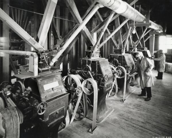 Two men operate machinery at Arcola Flour Mills. The equipment is powered by an International PD-40 Diesel power unit.