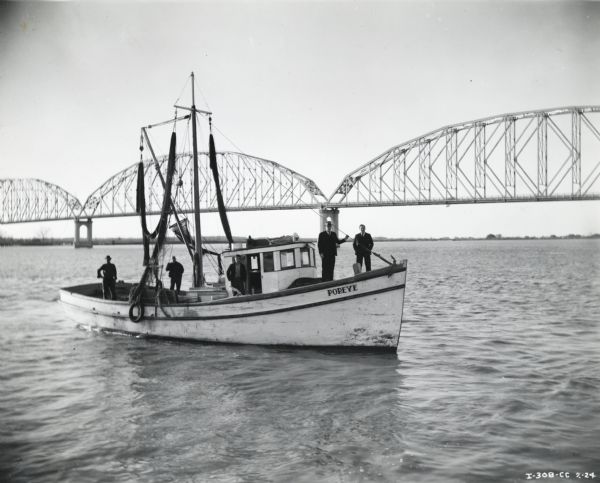 The boat <i>Popeye</i> floats in front of a bridge carrying five male passengers. The boat was powered by an International PD-80 Diesel power unit owned by St. Mary's Seafood Products.