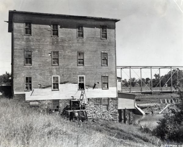 Field mill powered by an International PD-40 power unit. The power unit was owned by Walter Brown; a bridge and a body of water are to the right of the building.