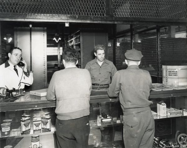 Two male customers stand at the parts counter of International Harvester's New York Manhattan truck branch. An employee behind the counter speaks on the telephone while another helps a customer.