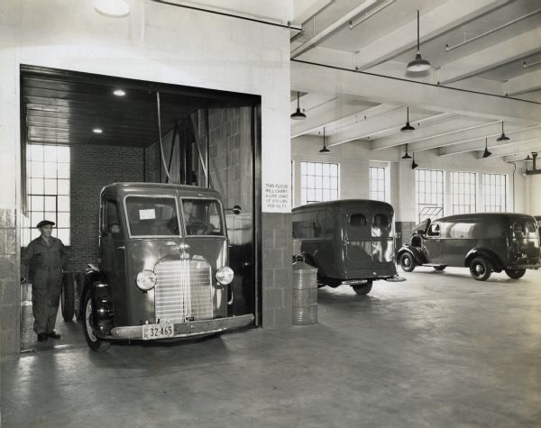 A man stands beside a truck in the new truck department on the third floor of International Harvester's Manhattan branch. Additional trucks are parked in the showroom.