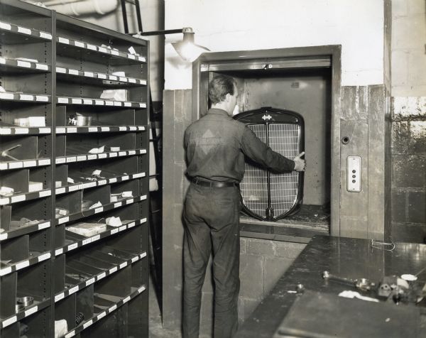 Repairs helper Thomas K. Chalmers handles a truck grille in a dumb waiter or service elevator in the parts department on the first floor of International Harvester's Manhattan truck branch. Shelves of smaller parts are vin the left foreground.