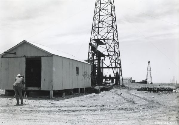 A photographer in the foreground takes a picture of two oil wells powered by an International PA-50 power unit and owned by Lee Petroleum Corporation.