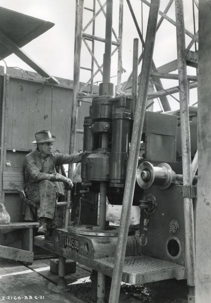 A man sits on the back of an International D-346-F truck outfitted with a core-drilling and shallow-well-drilling rig. The truck was also fitted with an International PA-50 power unit.