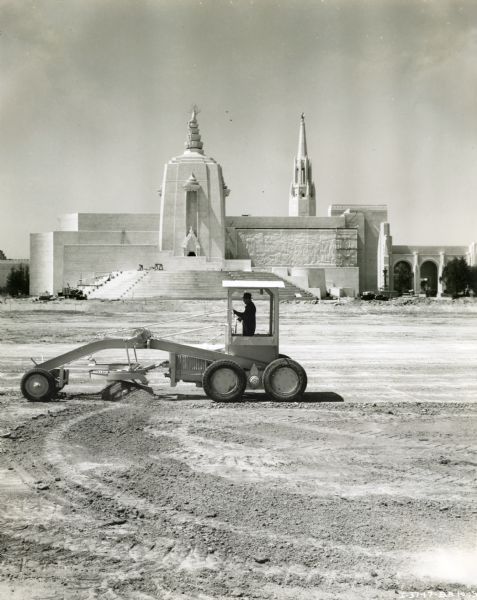 A man operates an Adams Motor Grader #102 owned by Eaton & Smith at the back entrance of the San Francisco World's Fair. The motor grader was powered by an International power unit.