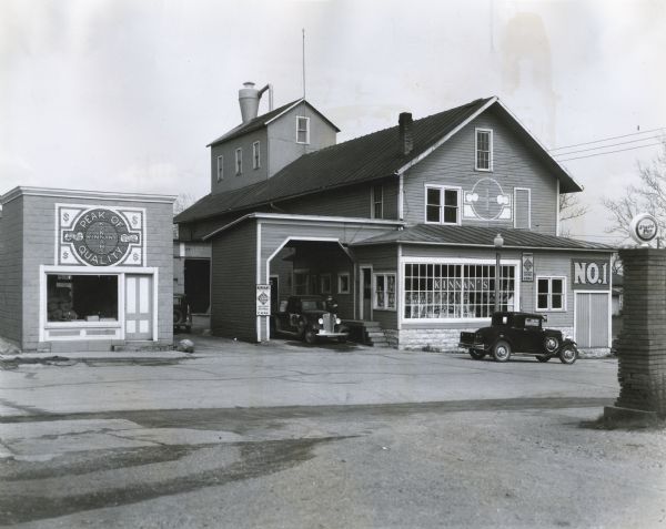 Exterior view of the front of the Kinnan Brothers hay and grain dealers' store.  Two automobiles are parked near the storefront. An International PD-80 operates for 18 to 24 hours a day inside.