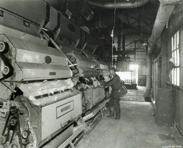 A worker stands at a machine inside a cotton gin owned by R.E. Cox.