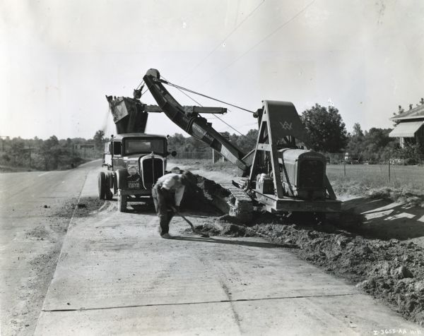 A man shovels dirt from a highway five miles north of Richmond next to an Austin-Western Badger shovel powered by a McCormick-Deering engine.  The equipment was owned and operated by R.K. Williams, contractor, of Richmond, Virginia.