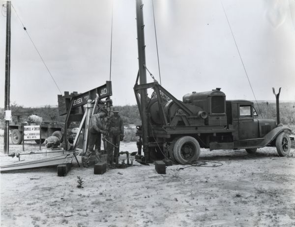 Two men work at an oil well site powered by an International Model P-30 power unit mounted on a truck.
