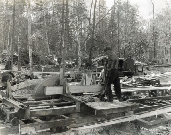 Workers saw logs at a sawmill site in a wooded area.  The equipment was powered by an International PD-80 power unit.