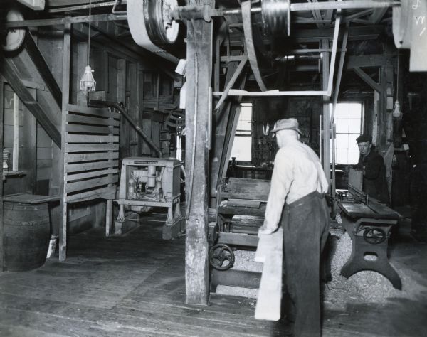 Workers use machinery inside a woodworking shop owned by H.P. Ghent.  An International P-12 power unit is on the left side of the room.