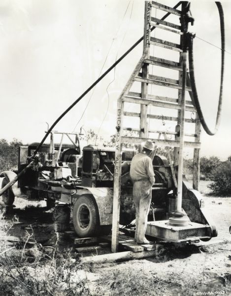 A.C. White, contractor, stands near a rotary water well rig powered by an International P-12 power unit mounted on a truck.