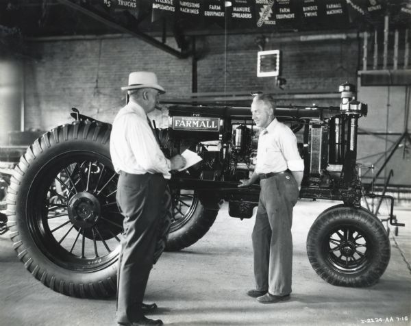 George Landaal, left, speaks to a customer in a showroom at Landaal Brothers, an International Harvester dealership. The men stand in front of a Farmall F-20 tractor. Pennants advertising farm machinery are hanging from the ceiling.