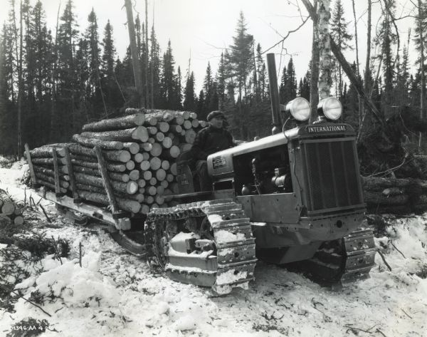 A man uses an International Model TD-35 TracTracTor (crawler tractor) to haul a sled loaded with logs. The photograph was taken in Fort Frances, Ontario, Canada.