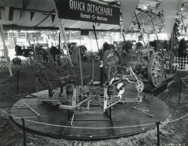 Farm implements mounted on a rotating circular platform near a Farmall F-12 tractor at the Indiana State Fair. The display was likely used to demonstrate "quick detachable" implements for use with the F-12.
