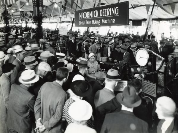 A crowd of people gathers around a McCormick-Deering binder twine-making machine for a demonstration beneath a tent at the Indiana State Fair.