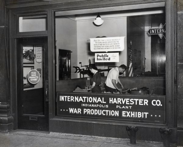 View through storefront window of a woman and a man working in an International Harvester Company war production exhibit at the Labor Recruiting Office. The demonstrators were from Harvester's Indianapolis plant.