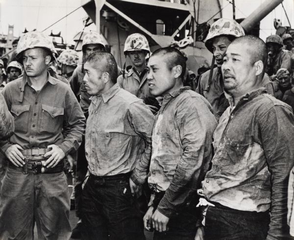 Three Japanese prisoners from the battle of Iwo Jima stand amongst American soldiers on a boat.