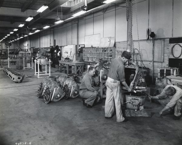 Three men work on the final assembly of Army air-borne invasion tanks in a temporary factory at International Harvester's Indianapolis branch house. Other workers are in the background.