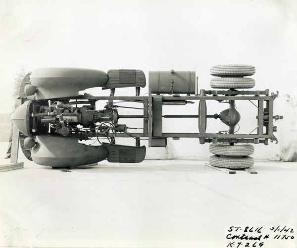 View of a K-7-269 International truck chassis, possibly used for military vehicles under a government contract. The truck chassis has been set on its left side for an undercarriage view.