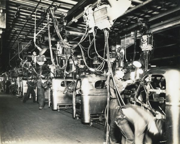 Factory workers wearing protective goggles use tools to assemble truck cabs on an assembly line at International Harvester's Springfield Works.