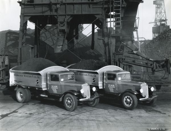 Two International C-55 trucks owned by the Milwaukee Western Fuel Company parked beneath a chute after being loaded with coal.