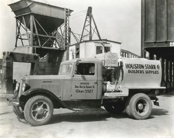 An International truck owned by the Houston-Starr Company parked in front of what appears to be a gravel chute and other storage buildings.