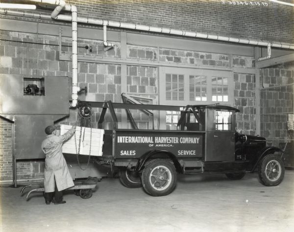A man loads a wooden crate onto the bed of an International sales and service truck using a chain hoist. The location is likely an International motor truck dealership or sales branch.