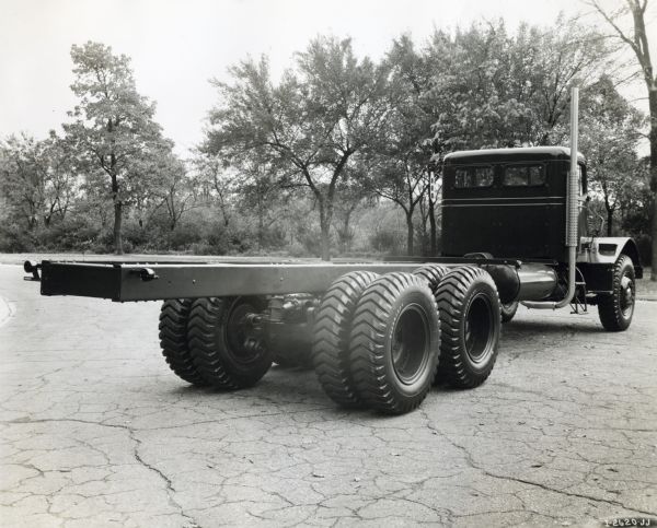 Three-quarter rear view of a heavy duty International truck. The truck is parked in a lot surrounded by trees.