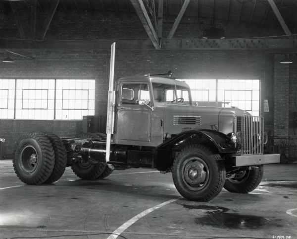 Three-quarter front view of the passenger side of an International truck parked inside of a brick building, possibly the Springfield Works factory floor.
