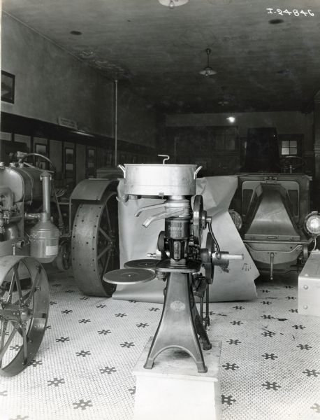 A Primrose cream separator standing on display in a showroom surrounded by a tractor, truck and farm equipment. The machinery may be on display at an International Harvester dealership.