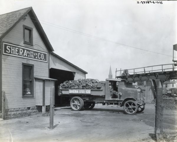 International heavy duty truck (possibly a model 103) loaded with coal  outside the Shera Coil and Oil Company building. In the background is a bridge and the steeple of a church building.