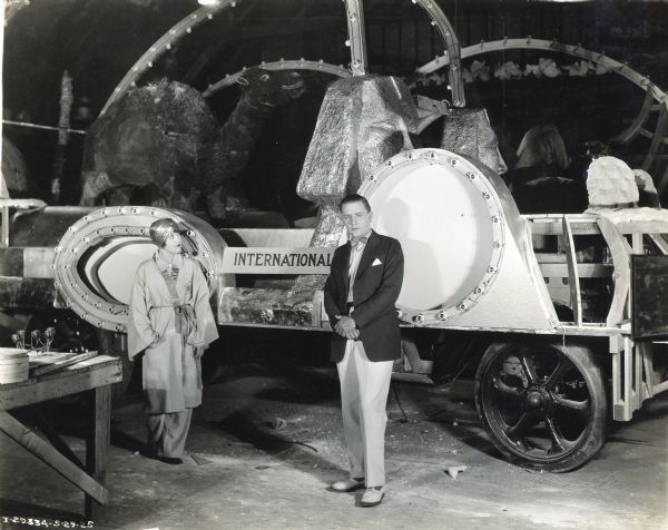 A man and a woman stand inside a building next to an International parade float decorated with a camel and what appear to be sphinxes.  The woman is in partial costume, wearing a metallic turban and a robe.