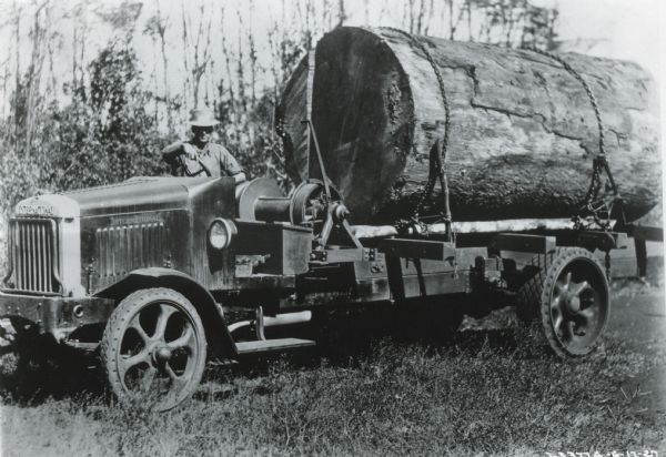 A man sits behind the wheel of an International truck with one large log loaded onto its bed.
