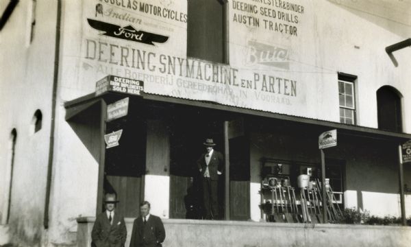 Men stand on and beside the porch or loading dock of an International Harvester (Deering) dealership in South Africa.
