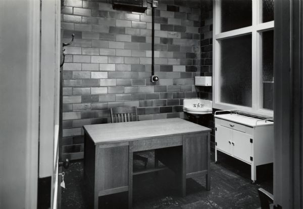 View of a desk, sink, and table arranged in a doctor's office in the First Aid Dispensary at International Harvester's Quad Cities Tank Arsenal.