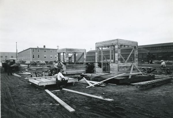 Men constructing guard towers at International Harvester's Quad Cities Tank Arsenal. Buildings and a vehicle are in the background.