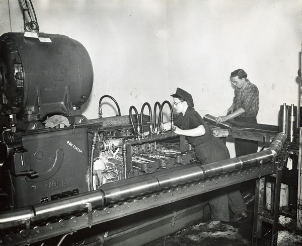 Factory workers at International Harvester's New Brighton Works turn 105mm shell cases on a piece of machinery.